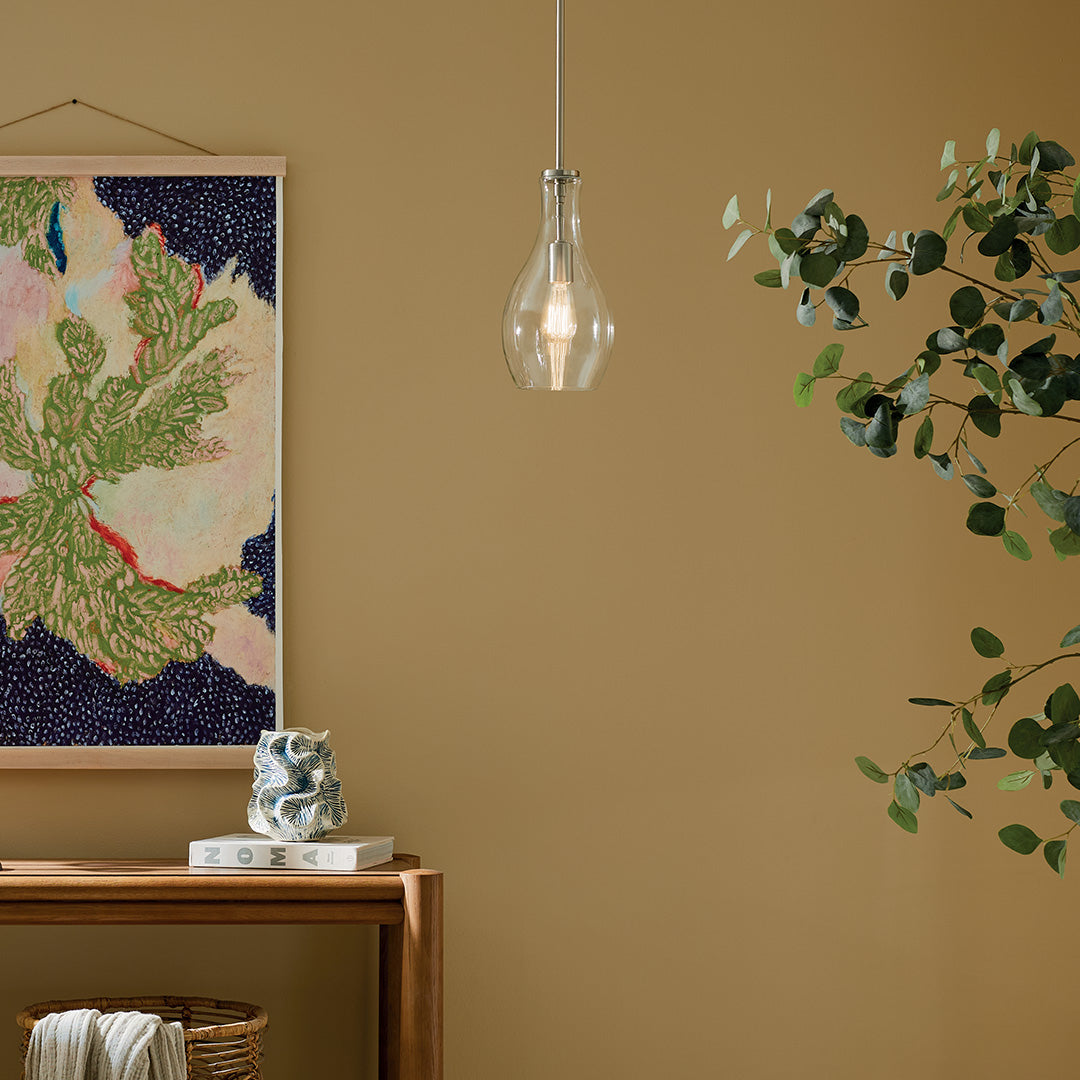 The Everly 13.75" 1-Light Bell Pendant with Clear Glass in Brushed Nickel hung in front of furniture and wall