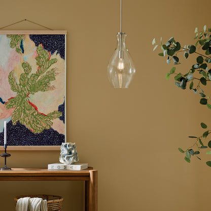 The Everly 17.75" 1-Light Bell Pendant with Clear Glass in Brushed Nickel hung in front of furniture and wall