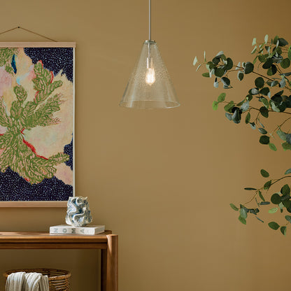 The Everly 15.5" 1-Light Cone Pendant with Clear Seeded Glass in Brushed Nickel hung in front of furniture and wall